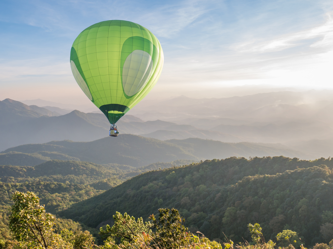 Ein grüner Heißluftballon, der über eine bewaldetet Landschaft fliegt. Weitsicht wird ermöglicht.