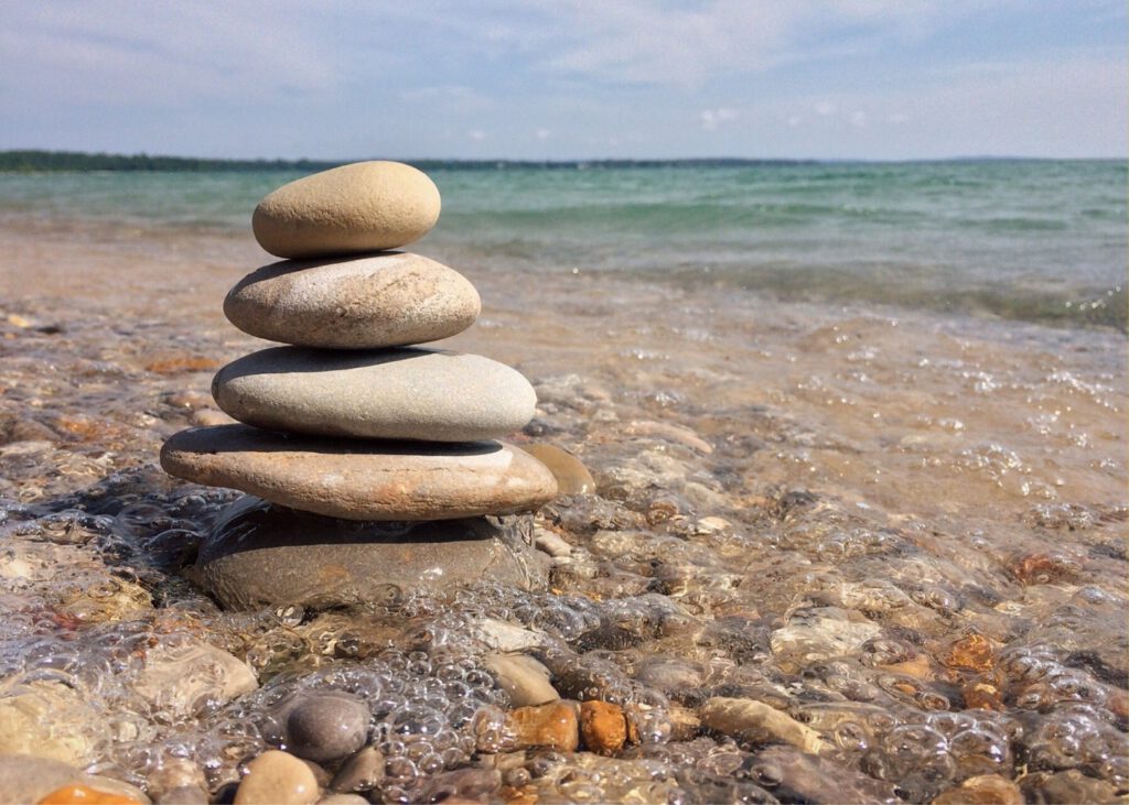 Fünf rundliche Steine, die übereinander liegen. Im Hintergrund Meer.