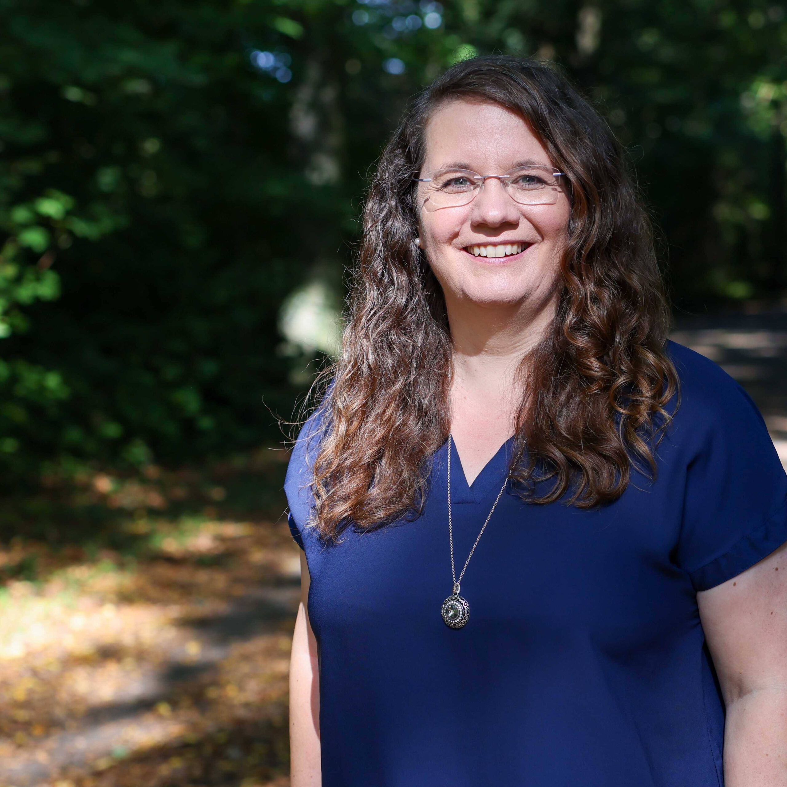 Katharina Temme - Coach, Supervisorin und Mediatorin aus Bergisch Gladbach - steht auf einem sonnenbeschienen Waldweg