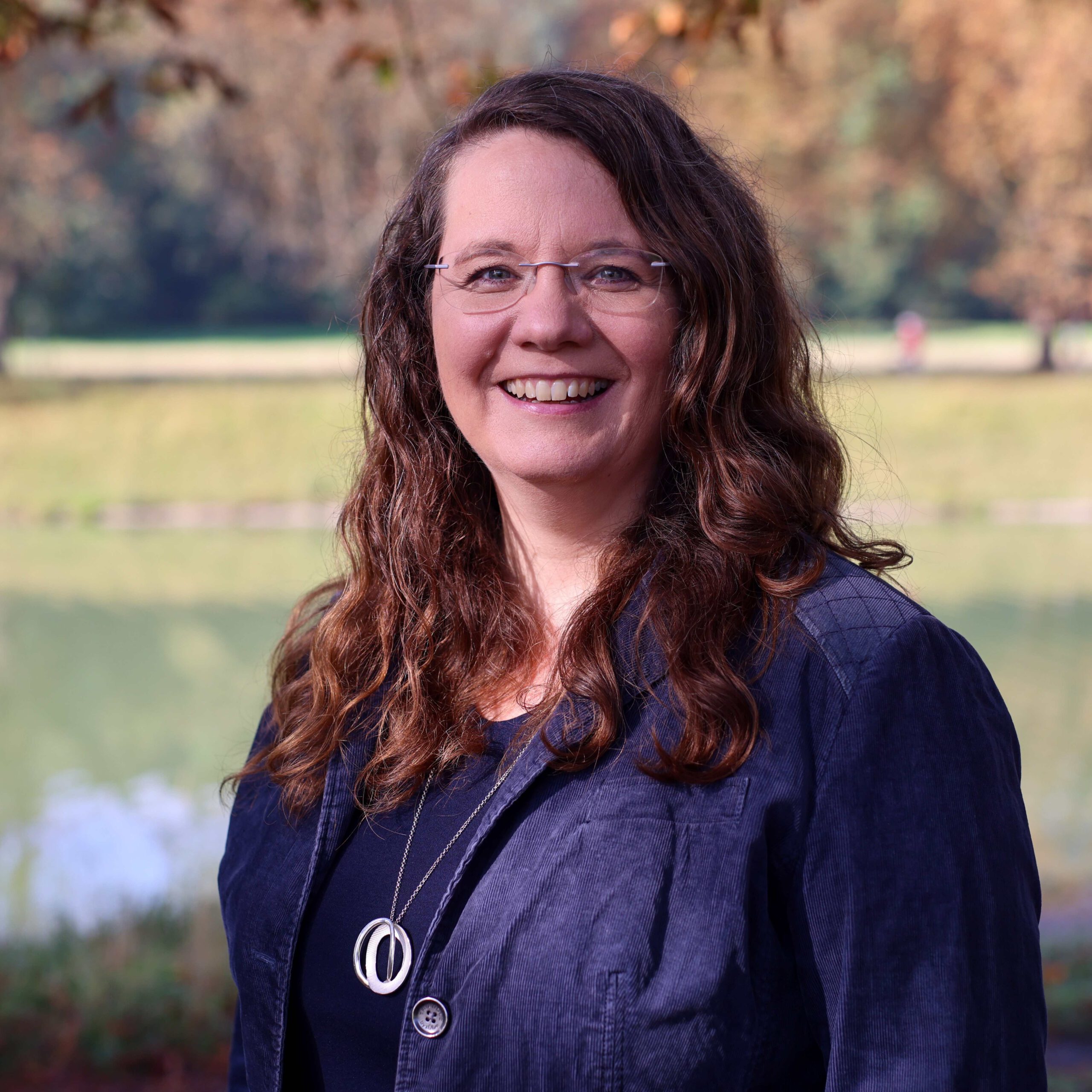 Coach und Mediatorin Katharina Temme vor einem Hintergrund aus Bäumen und Wasser.