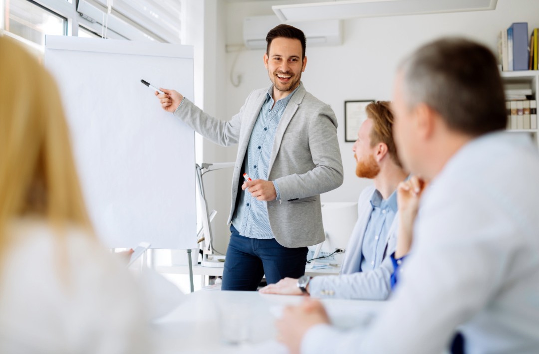 Ein Mann moderiert ein Meeting. Zwei Männer und eine Frau nehmen teil.