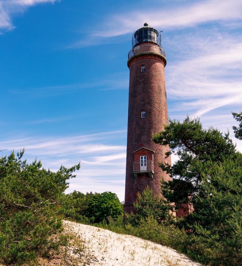 Ein Leuchtturm steht ist zwischen Dünen und flachen Kiefern zu sehen und steht für Klarheit und Sicherheit durch Coaching, Mediation und Teamentwicklung