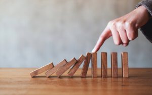 5 Dominosteine kippen, 4 Steine stehen, weil sie von einer Hand gestoppt werden – steht für Konfliktlösung und Konfliktbewältigung